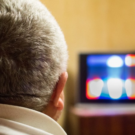 Photo of a man watching tv. We see the back of the man's head, plus the screen.