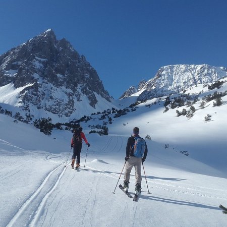 Photo on a snowscape, with a man in the foreground and a mountain in the background.