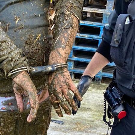 Photo of a man, covered in manure, with his hands handcuffed behind his back.