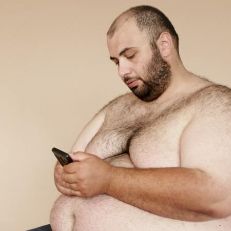 Photo of a fat man, topless, checking his phone.