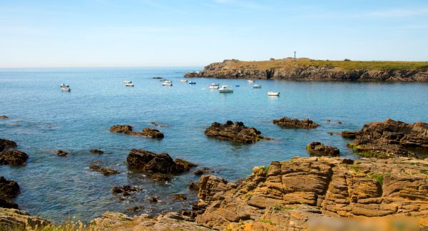 A photo from the Ile d'Yeux in France. It is a beautiful summer's day and we see rocky outcrops in a calm sea.
