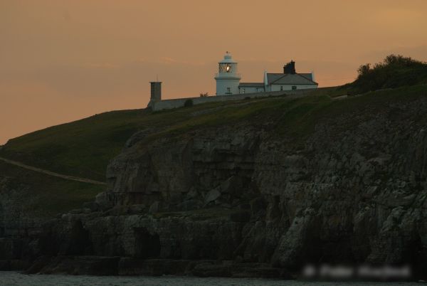 Photo of a lighthouse in the Purbecks, on the south coast of England. It is dusk and the light has just come on.