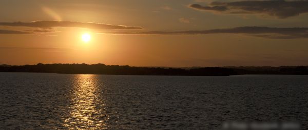 Photo across Poole Harbour, at sunset. The sun is rippling over the water.